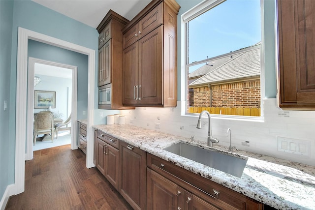 kitchen with light stone counters, dark wood-style flooring, backsplash, and a sink