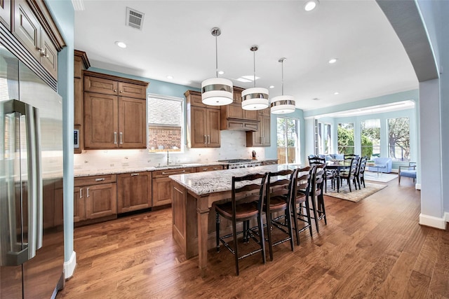 kitchen featuring visible vents, a breakfast bar, backsplash, wood finished floors, and appliances with stainless steel finishes