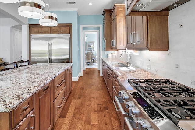 kitchen with light stone counters, wood finished floors, a sink, stainless steel appliances, and tasteful backsplash