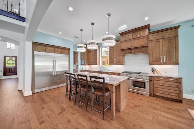 kitchen with light wood finished floors, a kitchen island, arched walkways, built in appliances, and tasteful backsplash