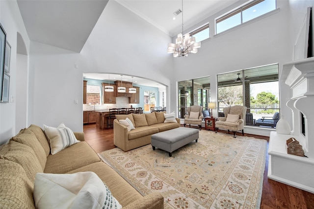 living area featuring visible vents, a fireplace with raised hearth, wood finished floors, arched walkways, and a chandelier