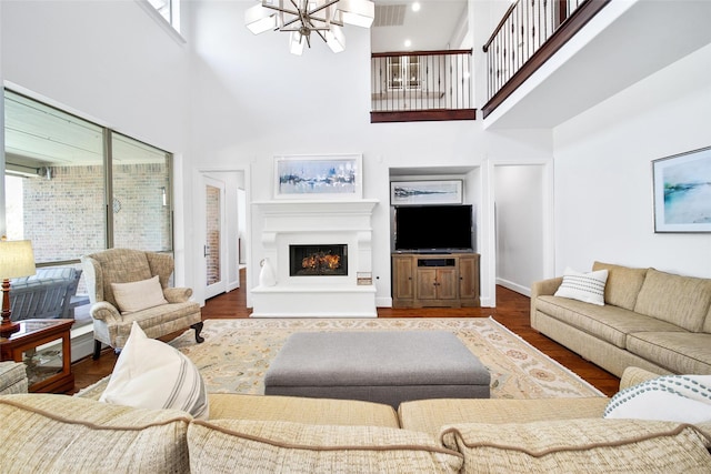 living room featuring visible vents, baseboards, a warm lit fireplace, an inviting chandelier, and wood finished floors