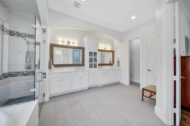 bathroom with visible vents, a shower stall, baseboards, double vanity, and a sink