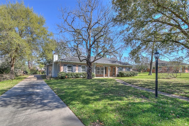 ranch-style home with a chimney, concrete driveway, a front yard, and brick siding