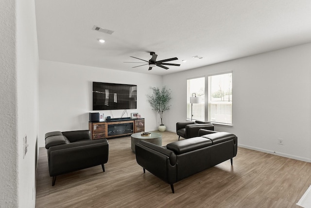 living room featuring visible vents, baseboards, wood finished floors, and a ceiling fan