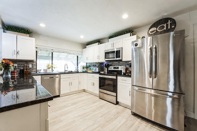 kitchen featuring light wood-type flooring, a sink, tasteful backsplash, appliances with stainless steel finishes, and white cabinets