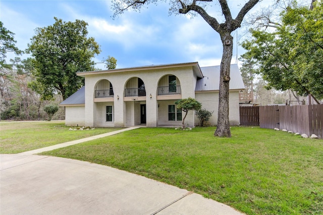 view of front of home with a front lawn, a balcony, fence, metal roof, and brick siding