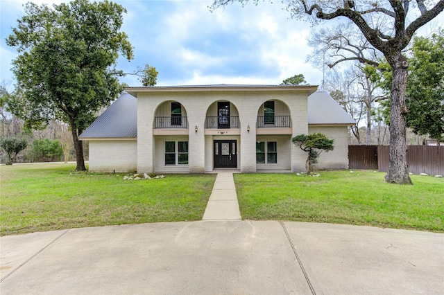 view of front facade featuring a front yard, brick siding, a balcony, and fence