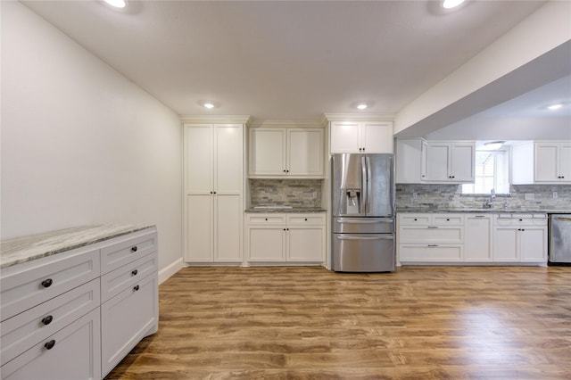 kitchen with light wood-type flooring, light stone counters, stainless steel appliances, white cabinets, and decorative backsplash