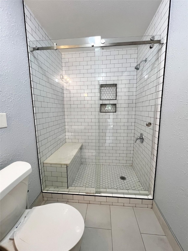 full bath with a stall shower, a textured ceiling, tile patterned floors, toilet, and a textured wall