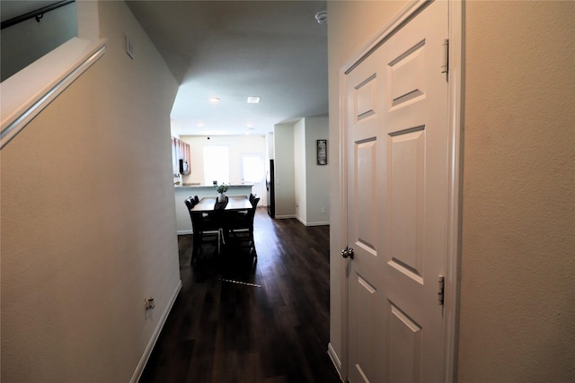 corridor featuring dark wood-type flooring and baseboards