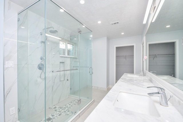 bathroom featuring a marble finish shower, visible vents, a walk in closet, recessed lighting, and a sink