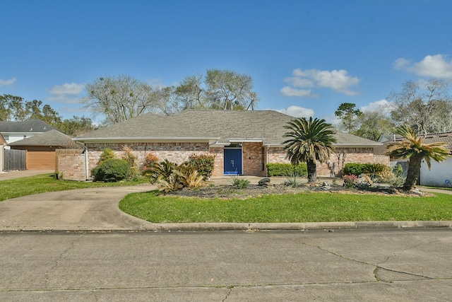 view of front facade with brick siding, a front lawn, fence, roof with shingles, and driveway