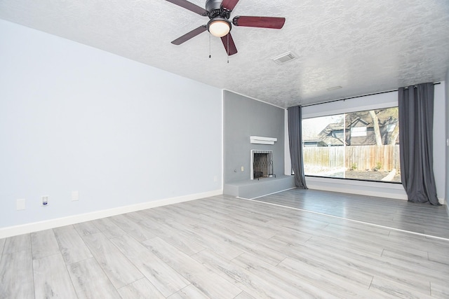 unfurnished living room with visible vents, a fireplace with raised hearth, baseboards, wood finished floors, and a textured ceiling