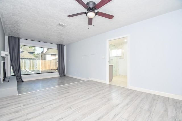 spare room with a ceiling fan, visible vents, wood finished floors, baseboards, and a textured ceiling