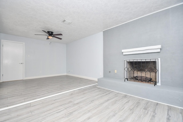 unfurnished living room with visible vents, a fireplace with raised hearth, wood finished floors, a textured ceiling, and a ceiling fan