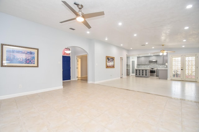 unfurnished living room with visible vents, arched walkways, baseboards, and ceiling fan