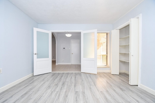 unfurnished bedroom featuring light wood-style floors, arched walkways, a closet, and baseboards