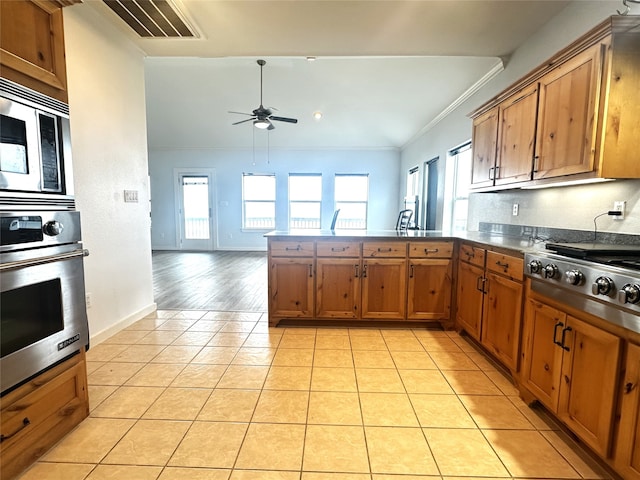 kitchen featuring open floor plan, light tile patterned floors, brown cabinets, appliances with stainless steel finishes, and a peninsula