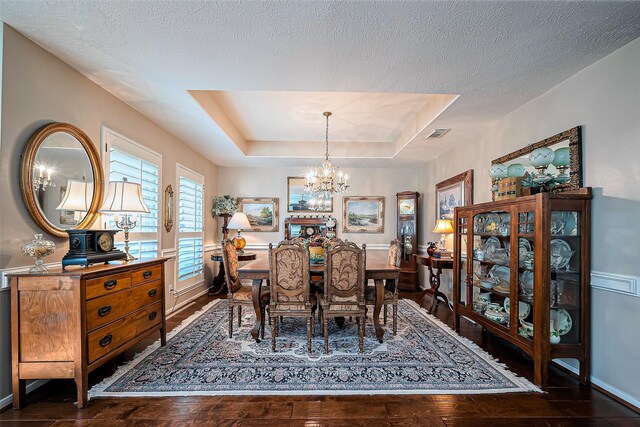 dining space featuring a chandelier, a textured ceiling, a raised ceiling, and hardwood / wood-style floors