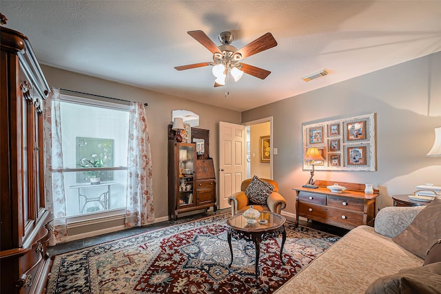 living area featuring visible vents, a textured ceiling, a ceiling fan, and baseboards