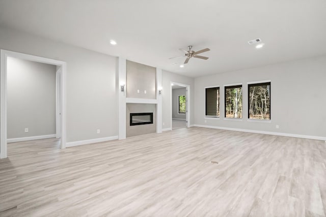 unfurnished living room featuring recessed lighting, visible vents, a glass covered fireplace, and light wood finished floors