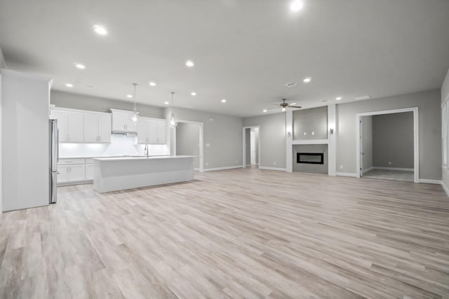 unfurnished living room with recessed lighting, light wood-type flooring, a glass covered fireplace, and a ceiling fan