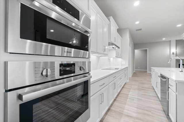 kitchen featuring visible vents, backsplash, dishwasher, light countertops, and white cabinetry