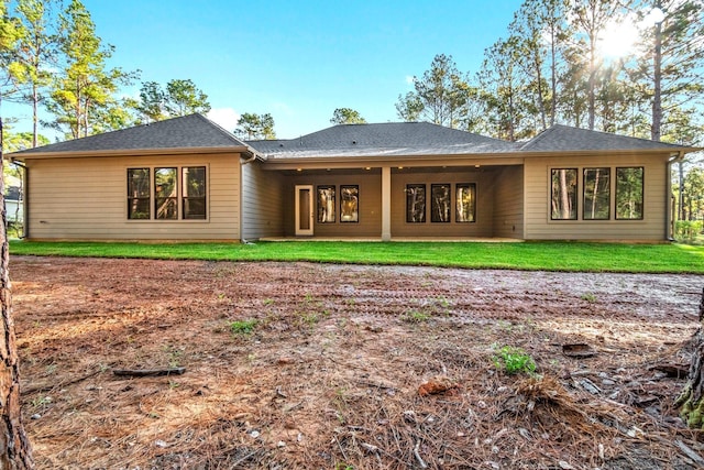 back of property with a shingled roof and a yard