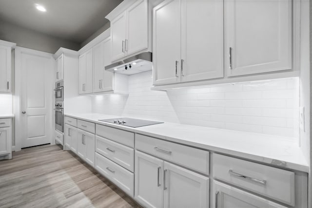 kitchen featuring light wood-type flooring, under cabinet range hood, white cabinetry, black electric stovetop, and tasteful backsplash