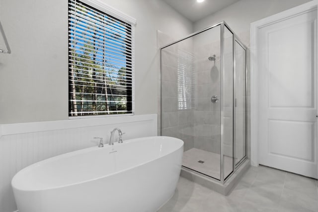 bathroom with a shower stall, a soaking tub, tile patterned floors, and wainscoting