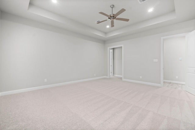 spare room featuring light carpet, a raised ceiling, and baseboards