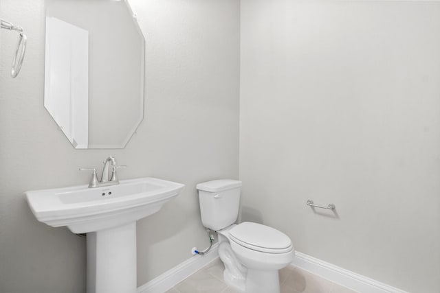 half bathroom featuring tile patterned flooring, toilet, baseboards, and a sink