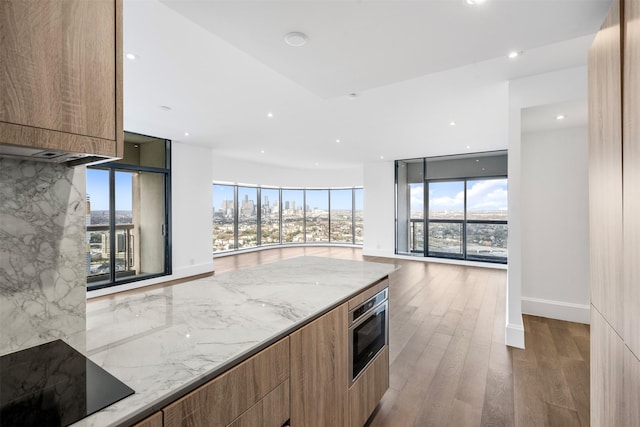 kitchen featuring light stone counters, wood finished floors, black electric stovetop, modern cabinets, and tasteful backsplash