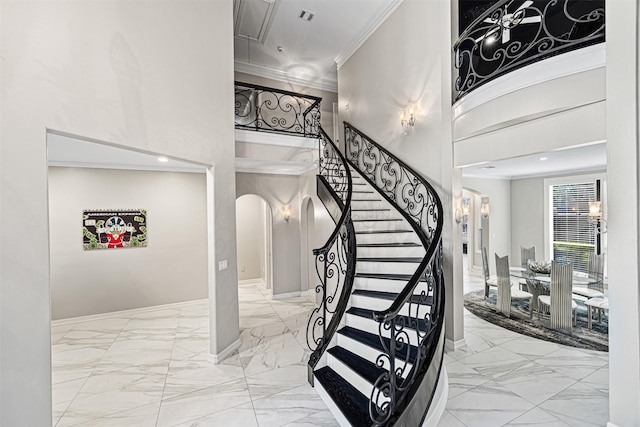 stairs featuring crown molding, arched walkways, marble finish floor, and a towering ceiling