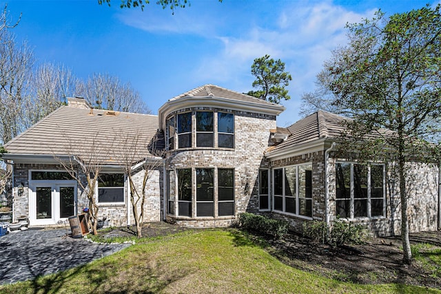 back of house featuring brick siding, a tile roof, a chimney, a yard, and a patio area