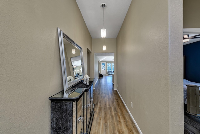 corridor featuring wood finished floors, baseboards, and a textured wall