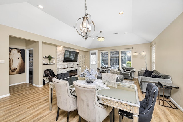 dining area featuring a fireplace, baseboards, light wood-style floors, and vaulted ceiling