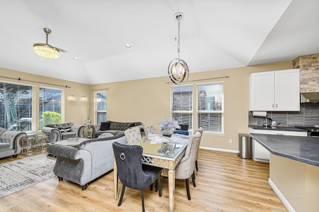 dining space featuring vaulted ceiling, light wood-type flooring, a wealth of natural light, and a chandelier