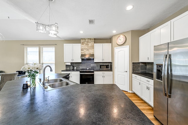 kitchen featuring visible vents, a sink, stainless steel appliances, dark countertops, and wall chimney exhaust hood