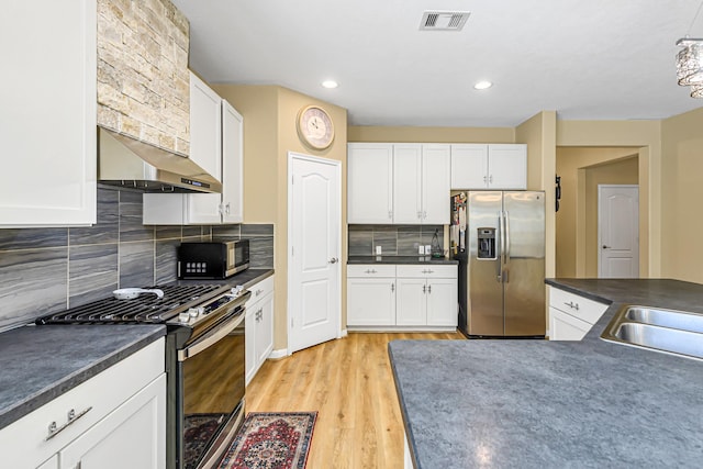 kitchen with dark countertops, white cabinets, under cabinet range hood, and stainless steel appliances