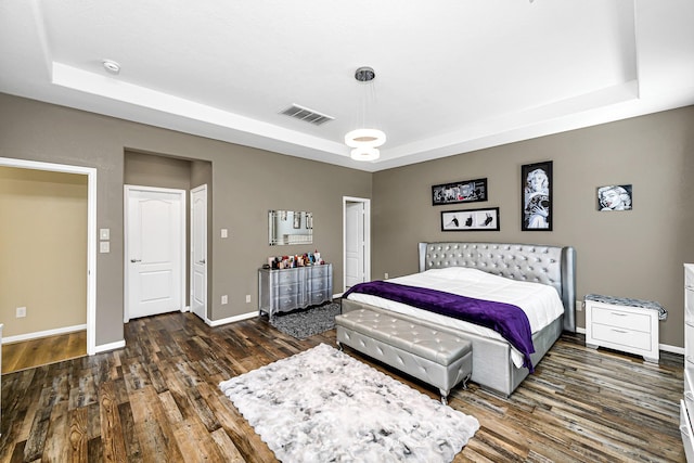 bedroom featuring visible vents, a raised ceiling, baseboards, and wood finished floors