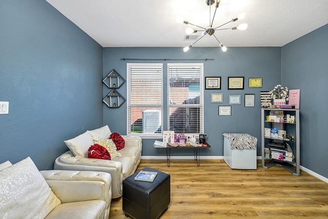 living area featuring a notable chandelier, visible vents, baseboards, and wood finished floors