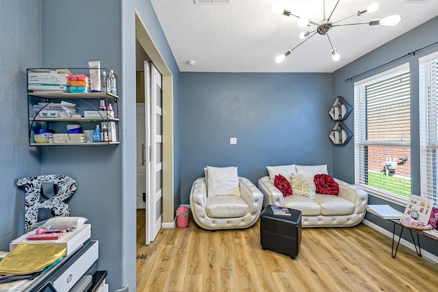 living area with visible vents, a notable chandelier, a textured ceiling, wood finished floors, and baseboards