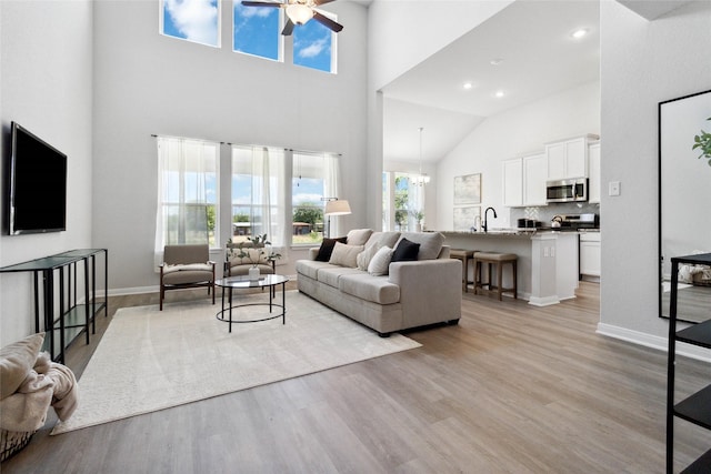 living room with light wood-type flooring, baseboards, a towering ceiling, and ceiling fan with notable chandelier