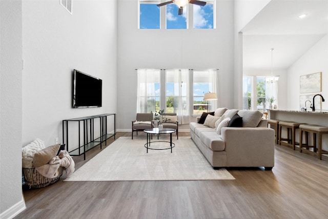 living area with ceiling fan with notable chandelier, wood finished floors, visible vents, and baseboards