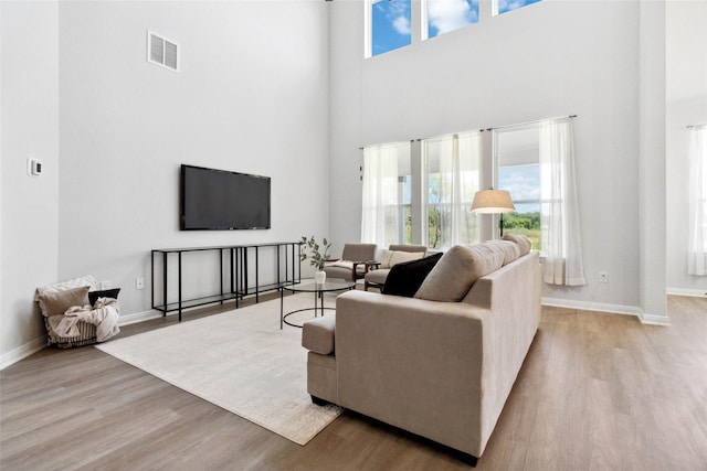 living area with visible vents, a high ceiling, baseboards, and wood finished floors