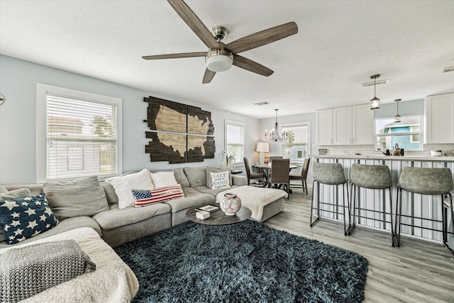 living area with visible vents, ceiling fan with notable chandelier, a textured ceiling, and light wood finished floors