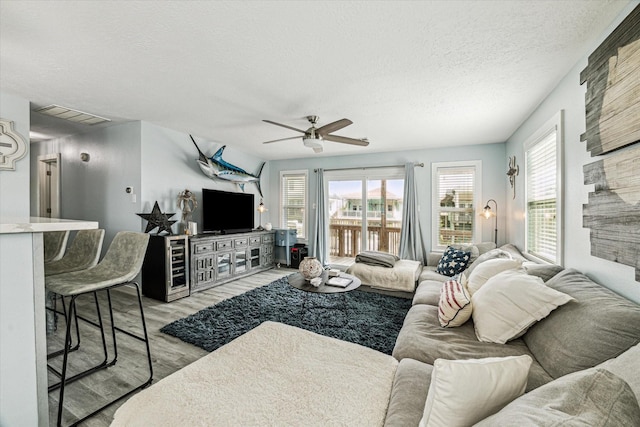 living room featuring light wood finished floors, visible vents, a textured ceiling, and a ceiling fan