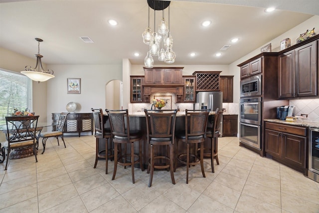 kitchen with glass insert cabinets, dark brown cabinetry, decorative backsplash, appliances with stainless steel finishes, and arched walkways